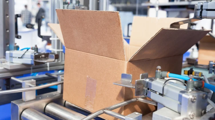 Una caja de cartón abierta sobre una cinta transportadora de rodillos en una fábrica.