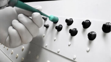 Technician applying sealant with a nozzle to a black rivet on a white aircraft surface.