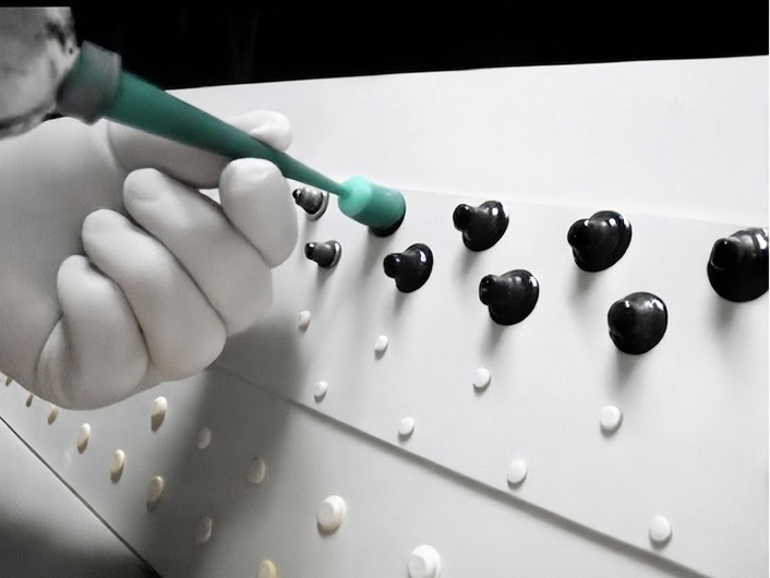 Technician applying sealant with a nozzle to a black rivet on a white aircraft surface.